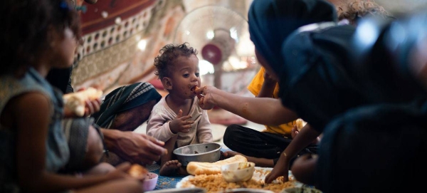 A one-year-old boy eats with his family in a displaced persons camp in Aden, Yemen.