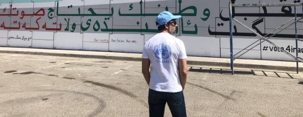 United Nations staff member Brenden Varma in front of a mural commissioned by the United Nations Assistance Mission for Iraq (UNAMI) to urge Iraqi citizens to vote.