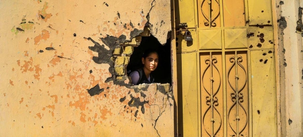 A young girl looks through a hole in the wall from damage from conflict in a school in Ramadi, Anbar Governorate, Iraq. 
