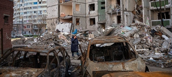 A woman walks past destroyed apartment buildings and vehicles in Chernihiv, Ukraine.