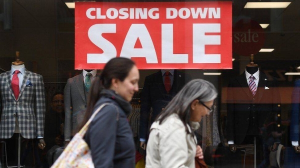 People walk past the closing down sign in a shop window.