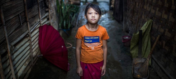 An young girl stands outside her home, in a displaced persons camp in Myanmar.