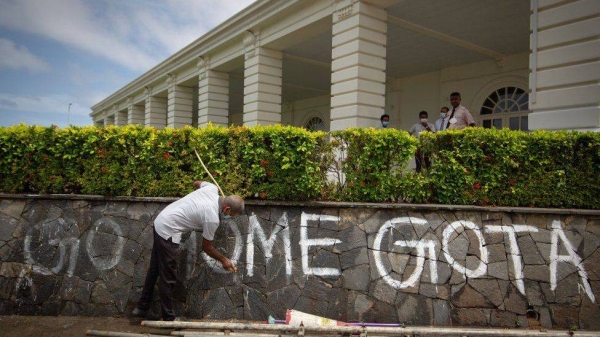 A staff member washes graffiti left behind by protestors from a hotel's compound wall near a protest site in Colombo.