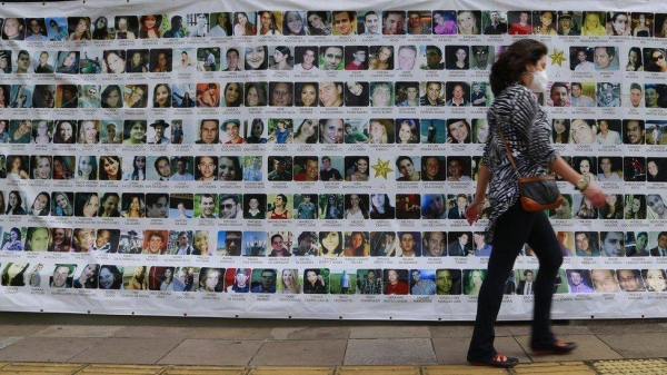 A person walks past a banner displaying the photos of the 242 people who died in the 2013 fire at the Kiss nightclub, during a trial against the accused, in Porto Alegre, Brazil, on December 1, 2021. (File)