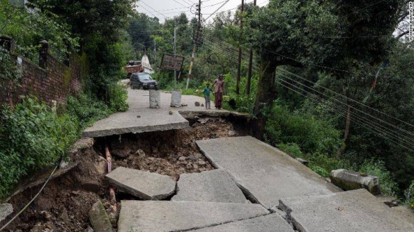 A woman and child look at a caved-in segment of a road damaged by heavy rain in Dharmsala, Himachal Pradesh state, India, on Sunday. 