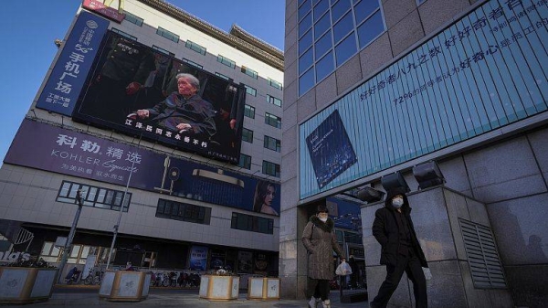 Residents walk by a live broadcast of the memorial service for late Chinese President Jiang Zemin. Tuesday.