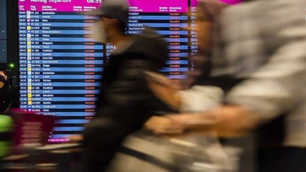 Passengers walk past the display board showing all flights as canceled during a warning strike at Berlin-Brandenburg BER Airport in Schoenefeld, Germany