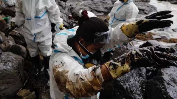 Filipino fishermen wearing protective suits collect oily waste along a beach in Pola