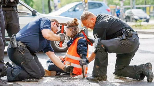 Police officers work to free a Letzte Generation (Last Generation) climate activist after he glued himself to the asphalt during a climate protest in Berlin, Germany. — courtesy Hannibal Hanschke/EPA-EFE/REX/Shutterstock