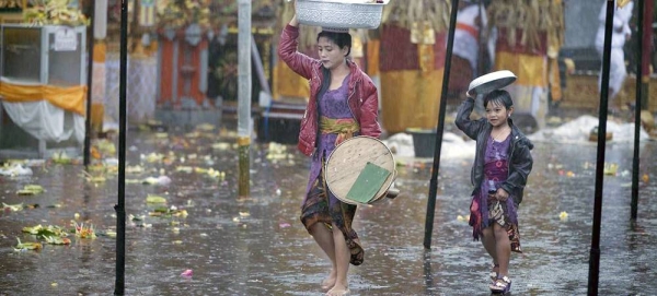 A mother and her daughter try to shield themselves from rain as they walk in a market. — courtesy ESCAP/Armin Hari