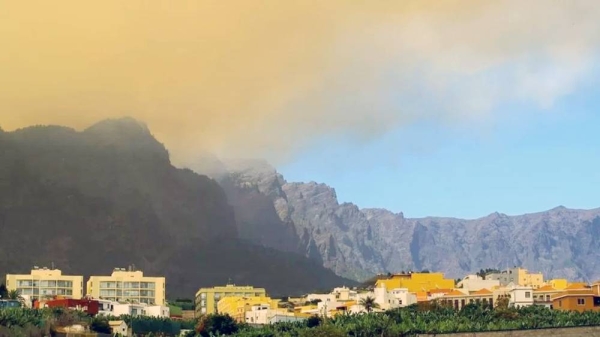 Smoke billows from a hill during a forest fire on the Canary island of La Palma. A row of buildings is visible in the foreground. — courtesy EPA