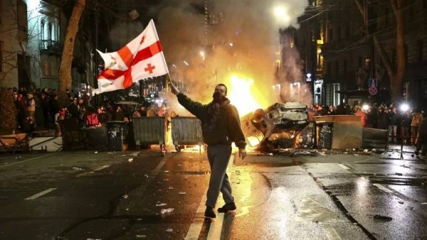 A man waves a Georgian national flag in front of a burning barricade as other protesters stand behind near the Georgian parliament building in Tbilisi, 9 March 2023.