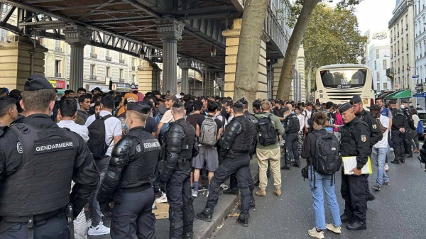 Police officers watch as homeless people, many of them migrants, wait to board a bus as part of a relocation scheme