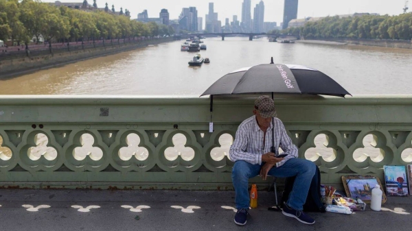 An artist sits beneath the shade of an umbrella on Westminster Bridge during hot weather in London on September 6