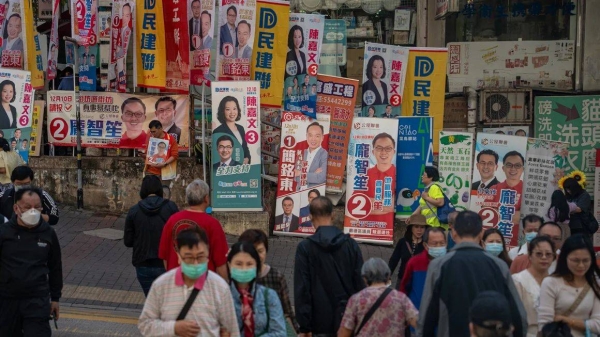 Residents cross the street in front of a wall of campaign banners for the district council elections in Hong Kong on December 10, 2023