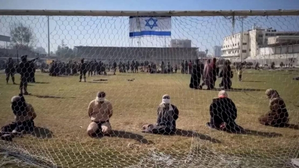 A still from a video appears to show Palestinian women and men blindfolded with their hands tied behind their backs as they sit on the grass in front of a soccer goal in the stadium