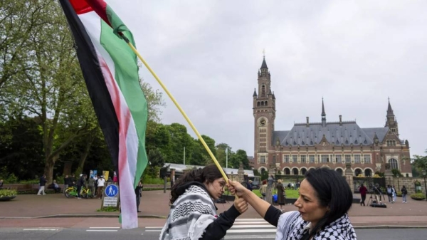 Two demonstrators wave the Palestinian flag outside the Peace Palace, rear, housing the International Court of Justice, or World Court, in The Hague, May 2024