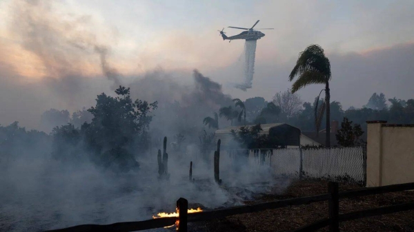 A helicopter drops water over a burning structure during a fast-moving wildfire in Moorpark, California