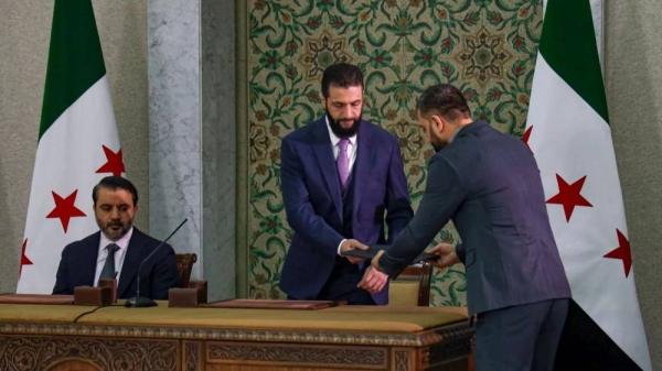 Syria's president Ahmad Al-Sharaa, center, prepares to sign a temporary constitution for the country in Damascus