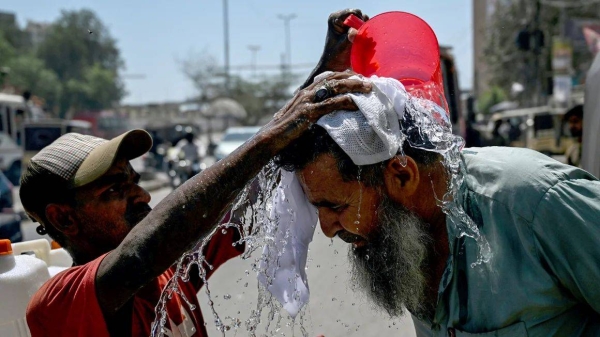 A volunteer pours water on a pedestrian's head to cool off during a hot summer day along a street in Karachi on April 5, 2025