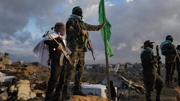 A boy holds an AK-47 rifle as he stands next to a Hamas militant ahead of the handover of four bodies of hostages to the Red Cross in Khan Younis, 20 February 2025
