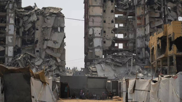 A group of Palestinians sit in the shade of their tent amid destroyed buildings on a hot summer day in Gaza City, 12 August, 2025
