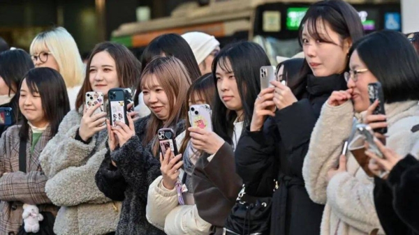 A group of Japanese women holding up their phones up to record and take photos of a scene in front of them