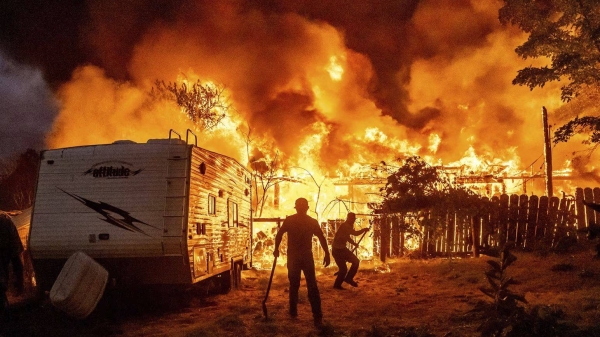 Residents work to stop flames from a burning home from spreading to a neighboring house as the 6-5 Fire burns through the Chinese Camp community in California on Tuesday
