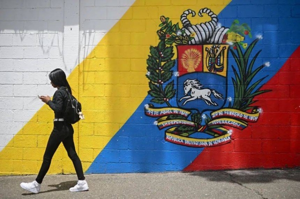 A woman walks in front of a mural with the Venezuelan coat of arms in Caracas on September 1