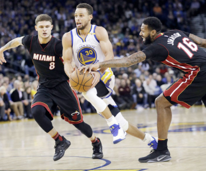 Golden State Warriors’ Stephen Curry drives between Miami Heat’s Tyler Johnson (L) and James Johnson during their an NBA game in Oakland Tuesday. — AP