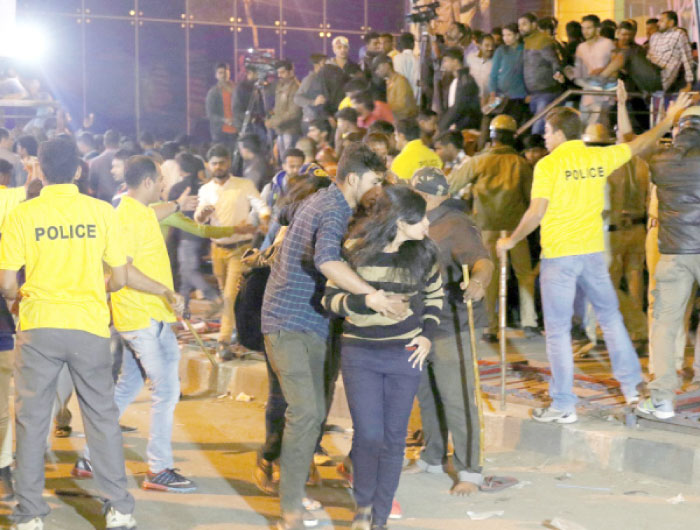An Indian man helps a woman, center, leave as police personnel try to manage crowds during New Year’s Eve celebrations in Bangalore on Sunday. — AFP