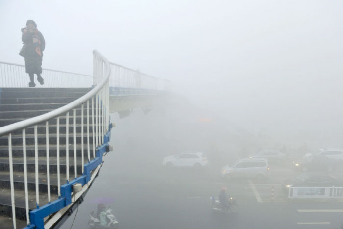 A woman uses a scarf to cover her for protection against air pollution walks on an overhead bridge in Fuyang in China’s Anhui province on Tuesday. — AP