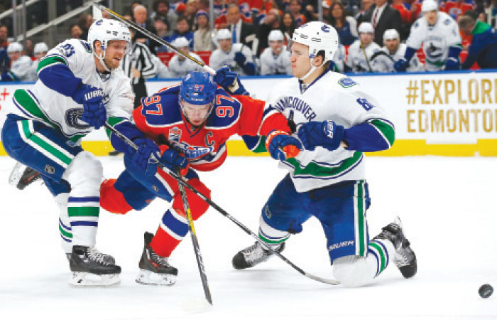 Vancouver Canucks’ defensemen Alex Edler (L) trips up Edmonton Oilers’ forward Connor McDavid (C) during their NHL game in Edmonton Saturday. — Reuters