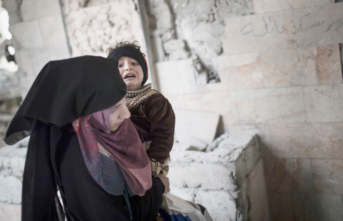 A woman carries her child as they flee through a destroyed train station during fighting between Iraqi security forces and Daesh militants, on the western side of Mosul. — AP
