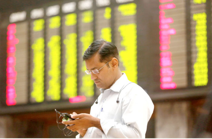 A man uses his cell phone as he stands in front of display board showing stock prices during a trading session in the halls of Pakistan Stock Exchange (PSE) Karachi, Pakistan, on Wednesday. — Reuters