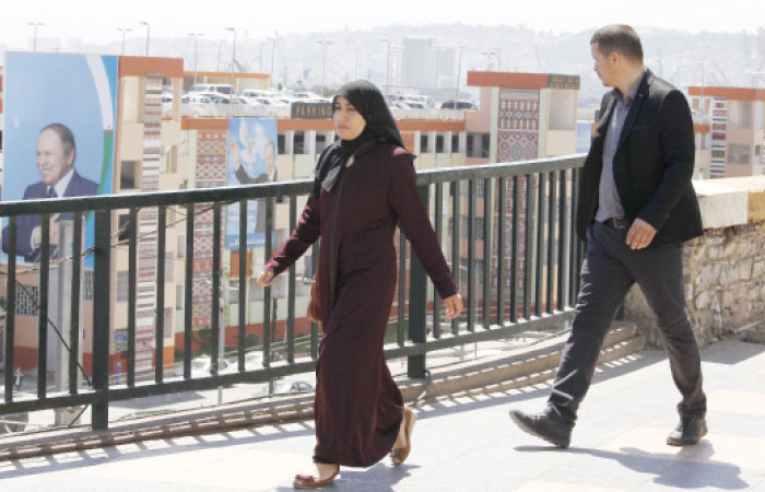 Pelople walk near portraits of Algerian President Abdelaziz Bouteflika in Algiers. — AP