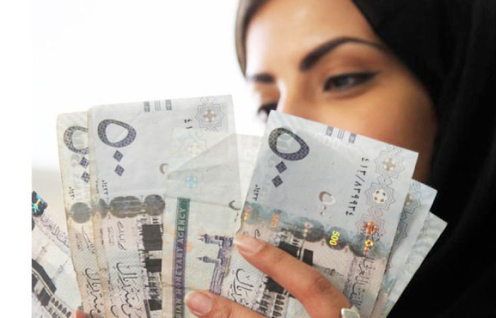 A Saudi woman poses with riyal banknotes at a money exchange shop in Riyadh. — Reuters