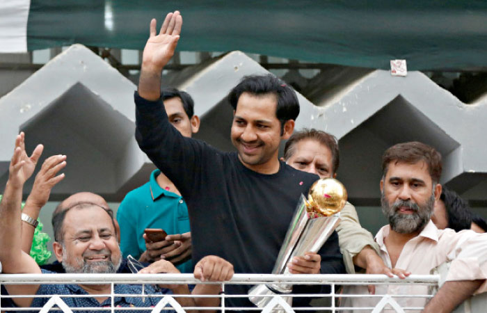 Pakistan’s Sarfraz Ahmed gestures to cricket fans with the ICC Champions Trophy upon his arrival at his house in Karachi Tuesday. — Reuters