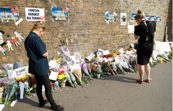 People stop to read tributes and look at plawers placed in the Finsbury Park area of north London on Tuesday, for the victims of a van attack on pedestrians nearby on Monday. — AFP